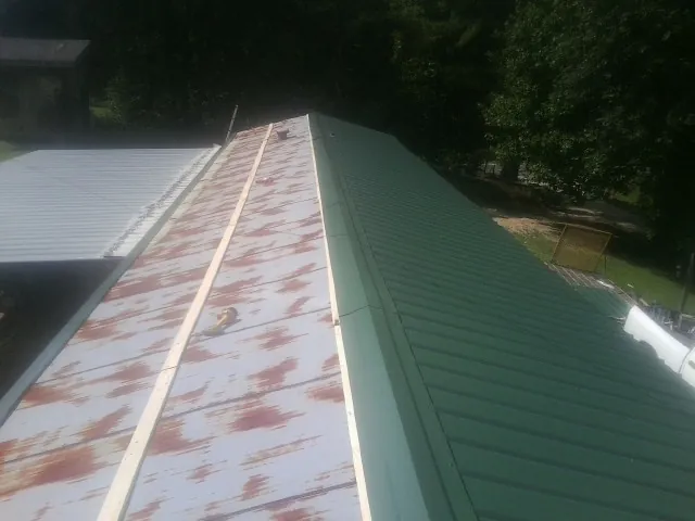 Old rusted panels beside newly installed green metal roofing — Wind Damage Roof Repair by Roofing Brothers in Blandinsville