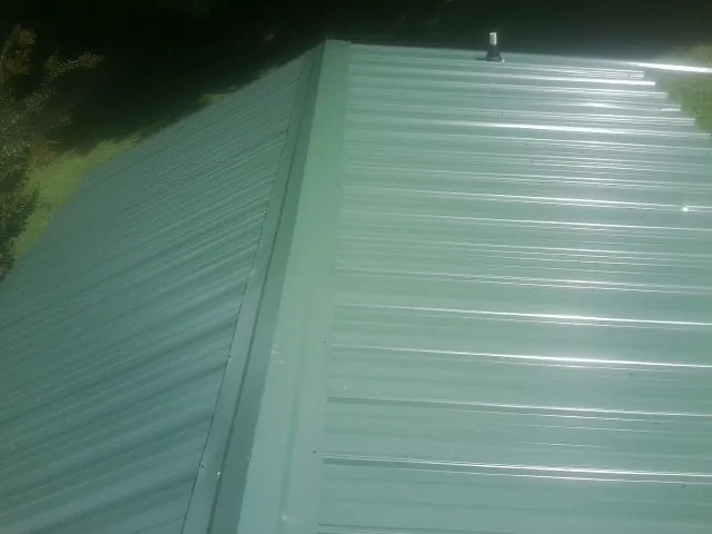 New green metal panels meeting at the ridge of a roof — Flat Roof Repair work by our crew in Blandinsville
