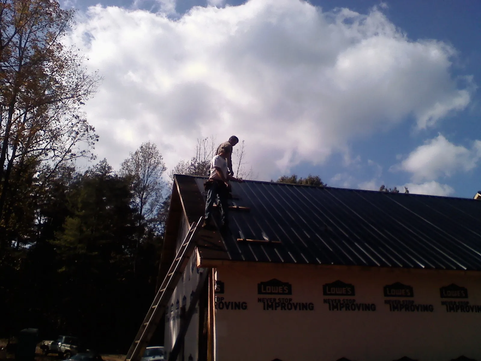 Roofer fastening dark metal panels high against a cloudy sky, from a Roof Inspection job in Blandinsville