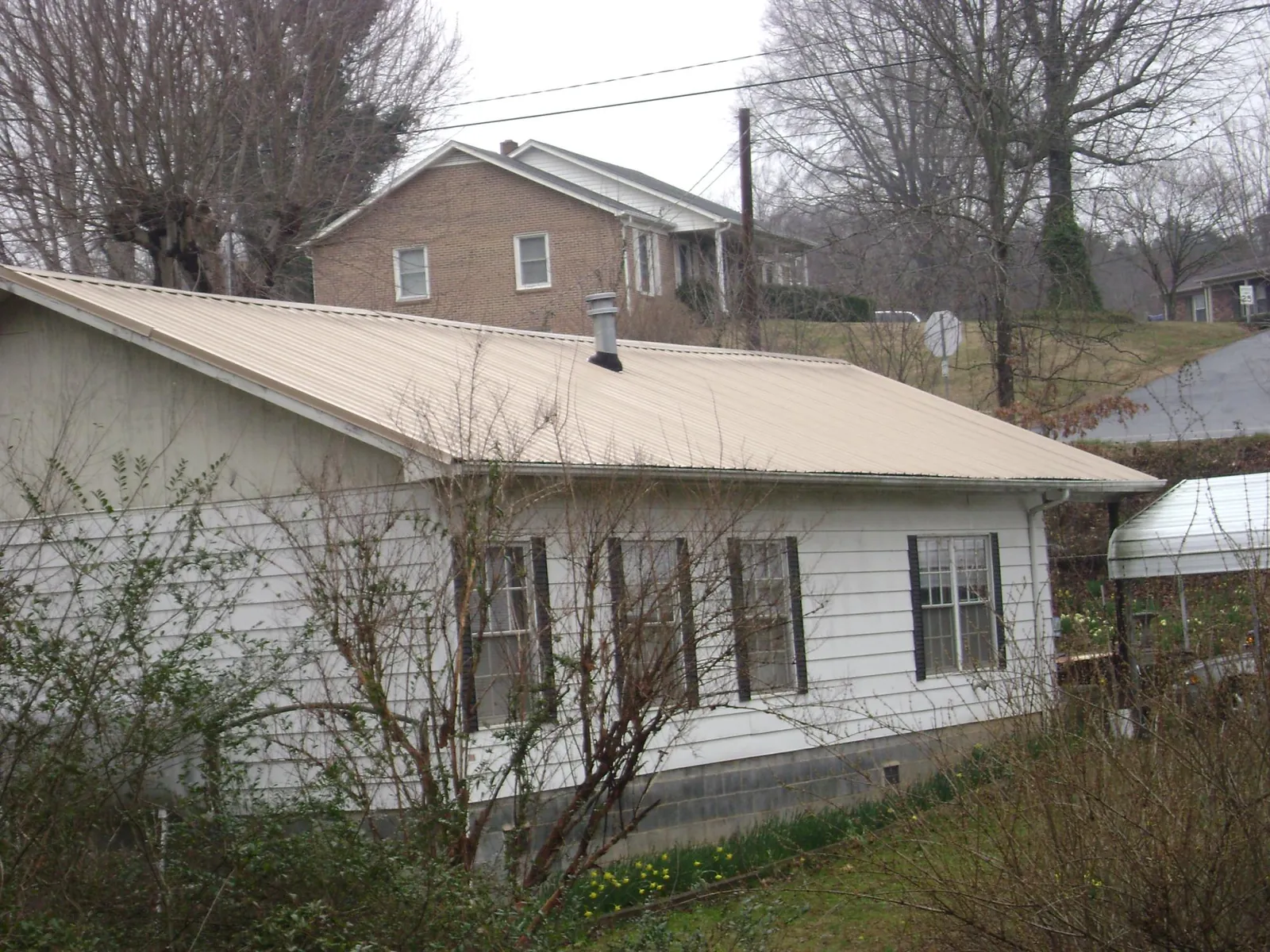 Tan metal roof on a white sided house set into a hillside — Commercial Roofing by Roofing Brothers in Blandinsville
